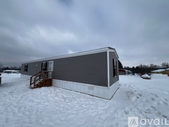A grey house with a brown staircase is surrounded by snow.