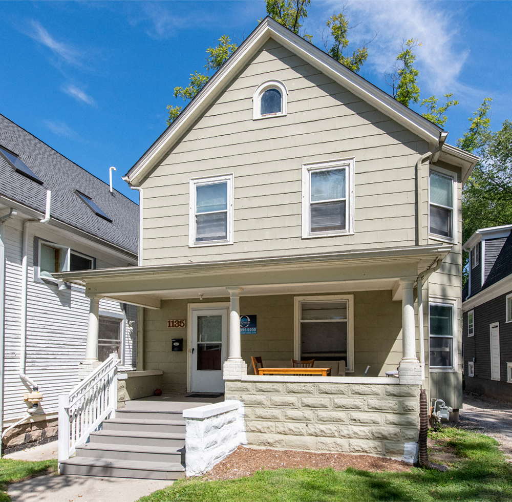 the front of a tan house with a porch and stairs