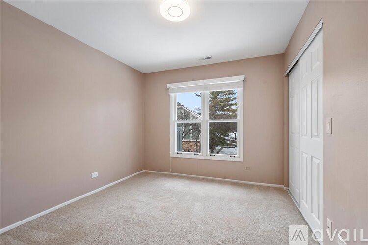 A room with a carpeted floor and a window showing a view of trees and a house.