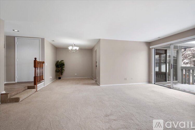 A spacious room with a carpeted floor and a staircase on the left side.