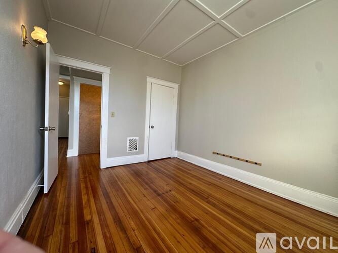 A room with wooden floors and white walls, with a door on the left and another door on the right.