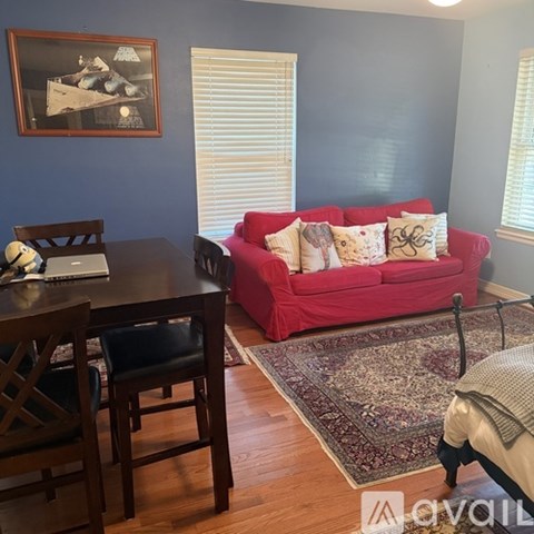 A red couch with pillows sits in a living room with a wooden table and chairs.