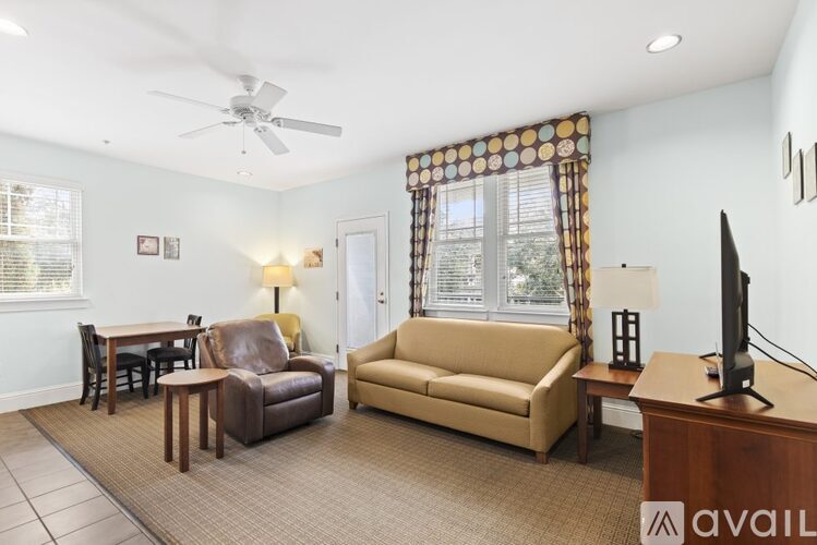 A living room with a brown sofa, a brown chair, a brown table, a television, and a fan.