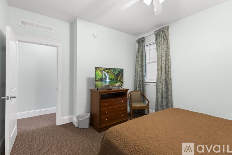 A bedroom with a bed, dresser, chair, and television.