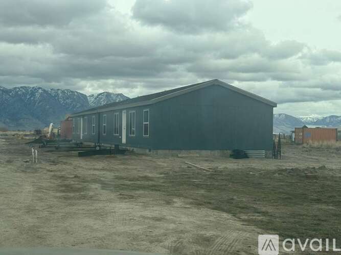 A grey building sits in a field with mountains in the background.