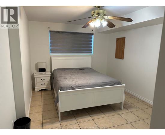 A bedroom with a bed, nightstand, and trash can.