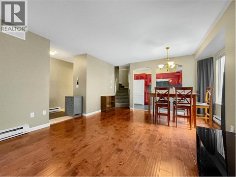 A living room with a wooden floor and a dining table with chairs.