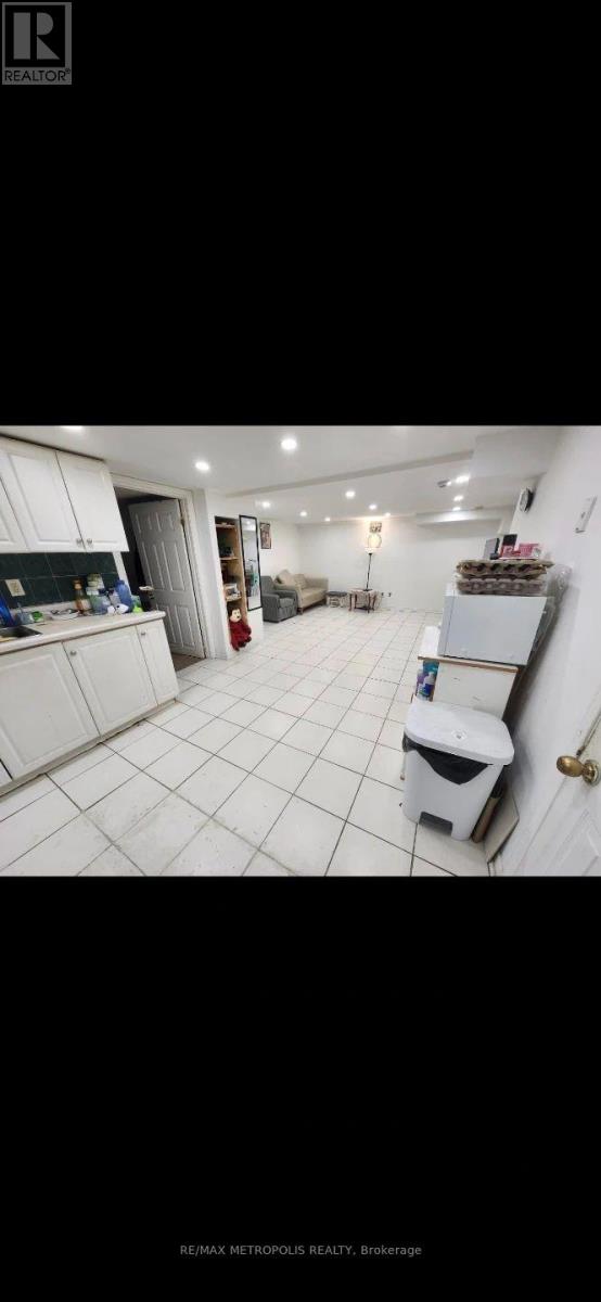 A white tiled kitchen with a white fridge and a white toilet.