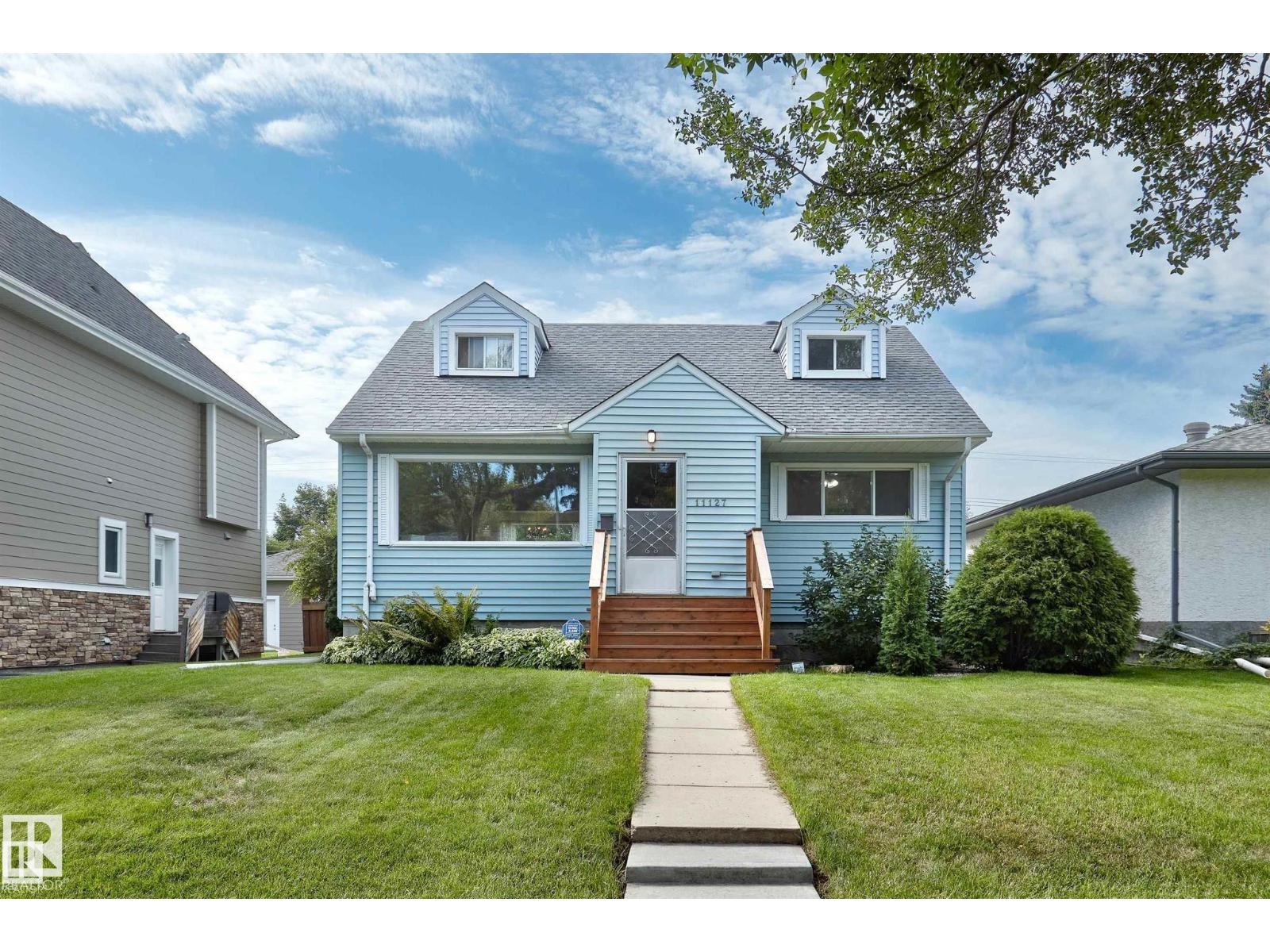 A blue house with a white door and windows is surrounded by a green lawn.