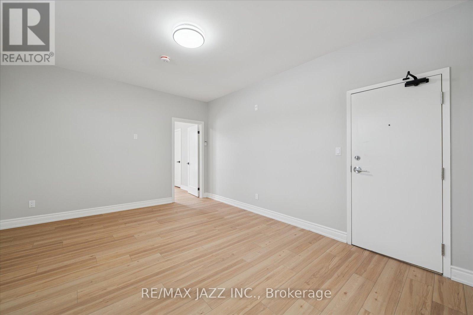 A room with wooden flooring and white walls, with a door on the right side.