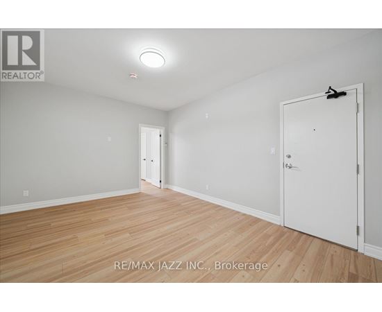 A room with wooden flooring and white walls, with a door on the right side.