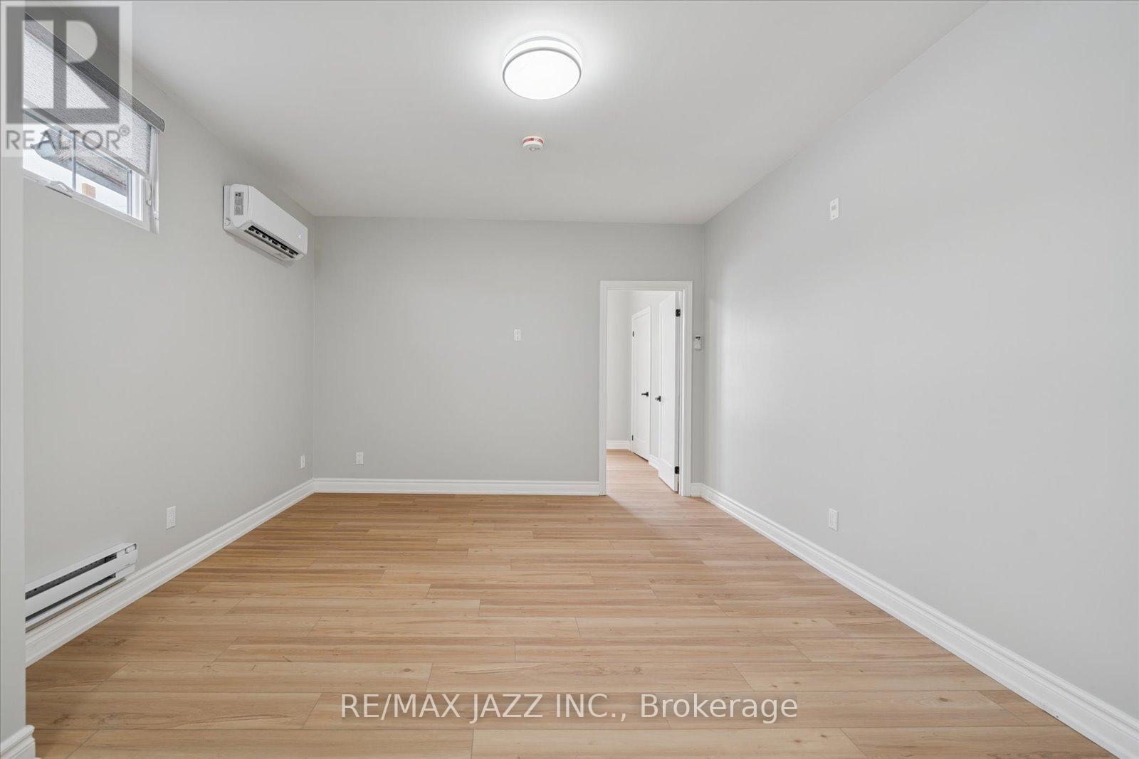 A spacious room with wooden flooring and white walls, featuring a brokerage sign.