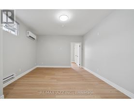 A spacious room with wooden flooring and white walls, featuring a brokerage sign.