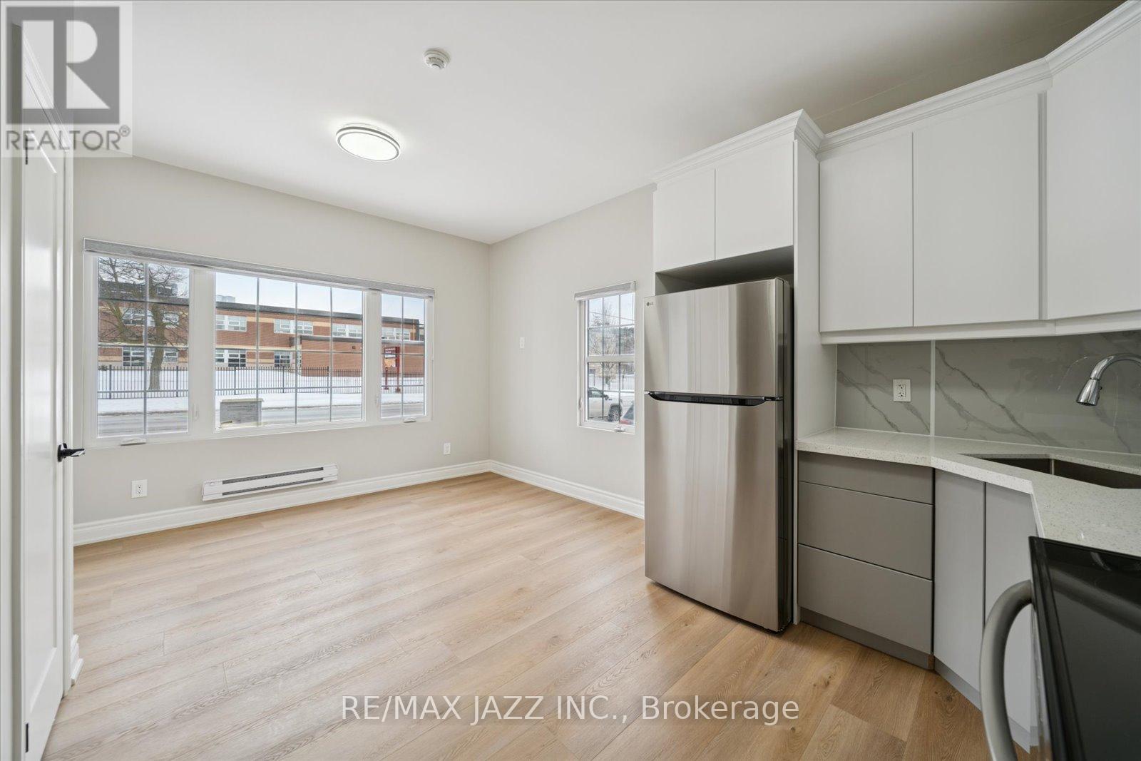 A kitchen with white cabinets and a refrigerator in a room with a window.