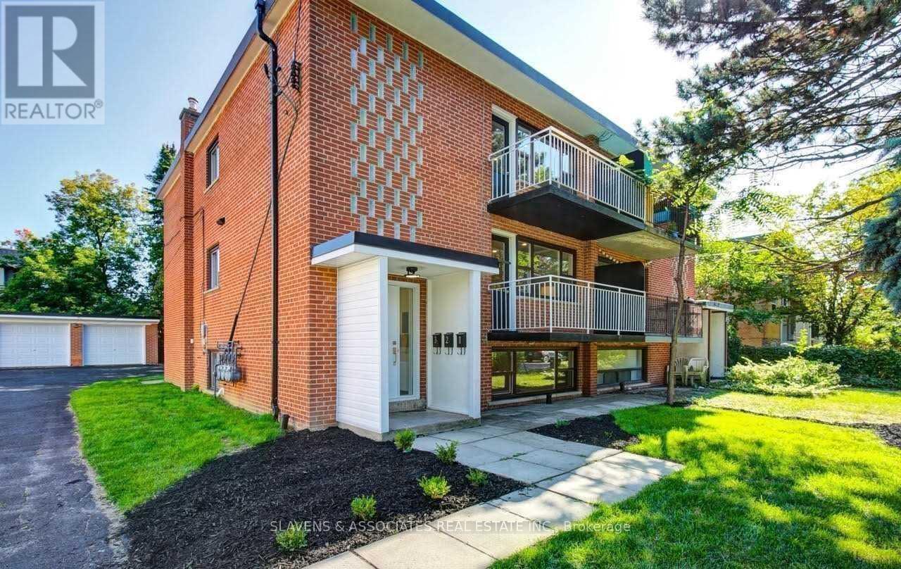 A red brick house with a balcony and a driveway in front.