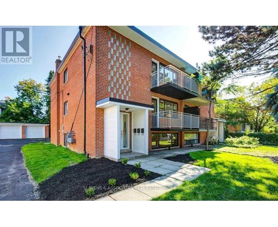 A red brick house with a balcony and a driveway in front.