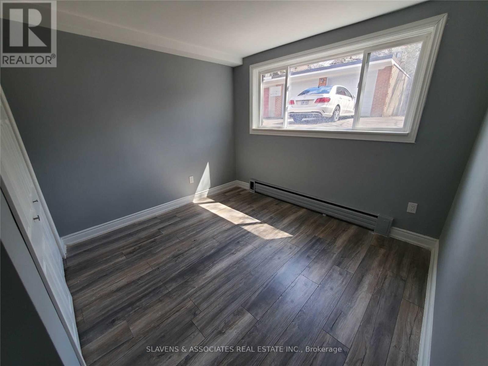 A room with wooden flooring and a window showing a car and houses outside.