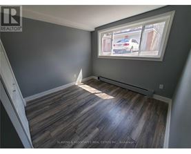A room with wooden flooring and a window showing a car and houses outside.