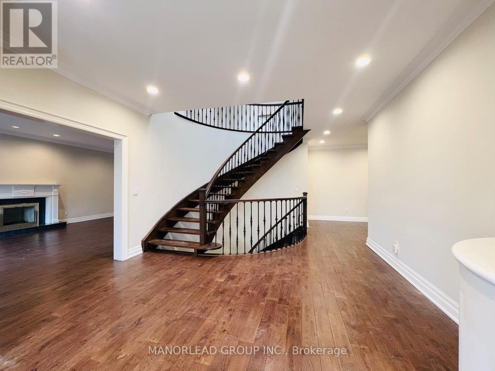 A spacious room with a wooden floor and a staircase with a black railing.