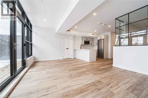 A spacious room with wooden flooring and a kitchen area in the background.