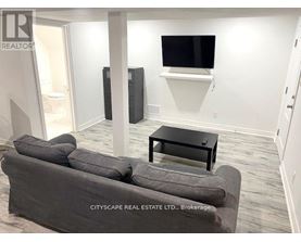 A living room with a grey couch, a black coffee table, and a flat screen TV mounted on the wall.