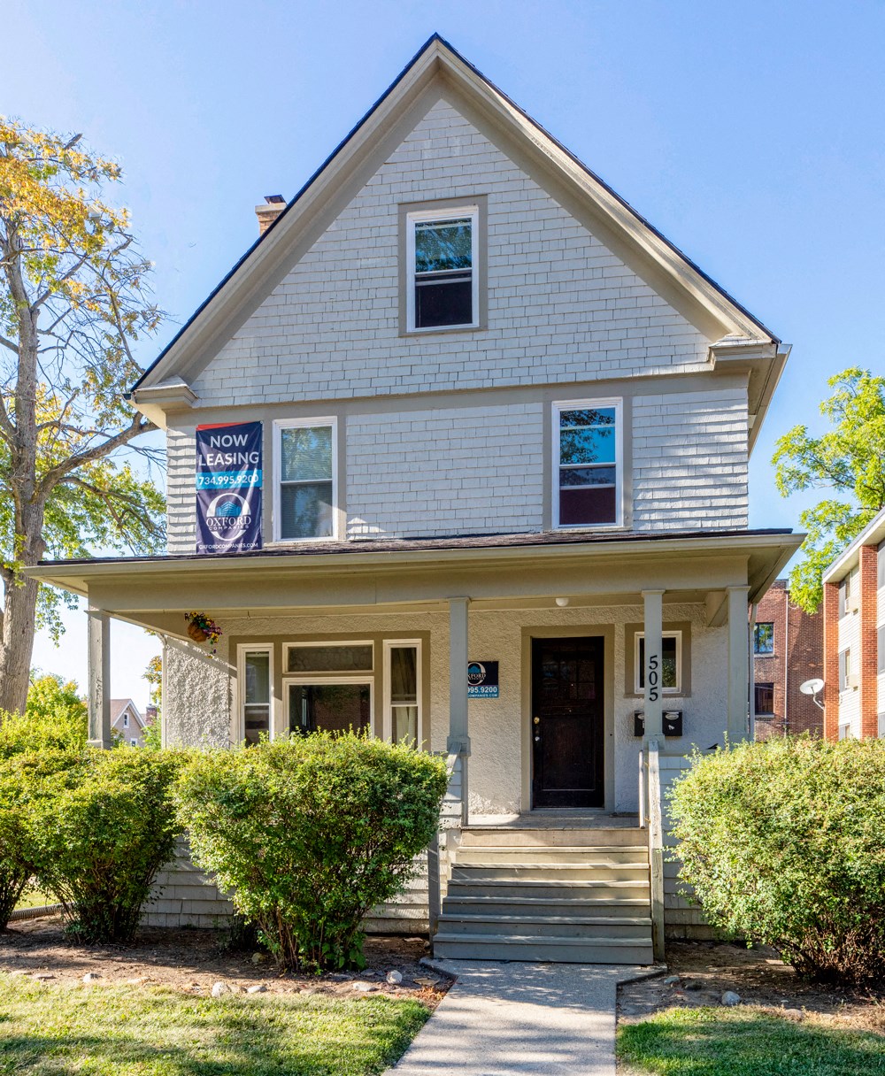 the front of a white house with a porch and a sign in the window