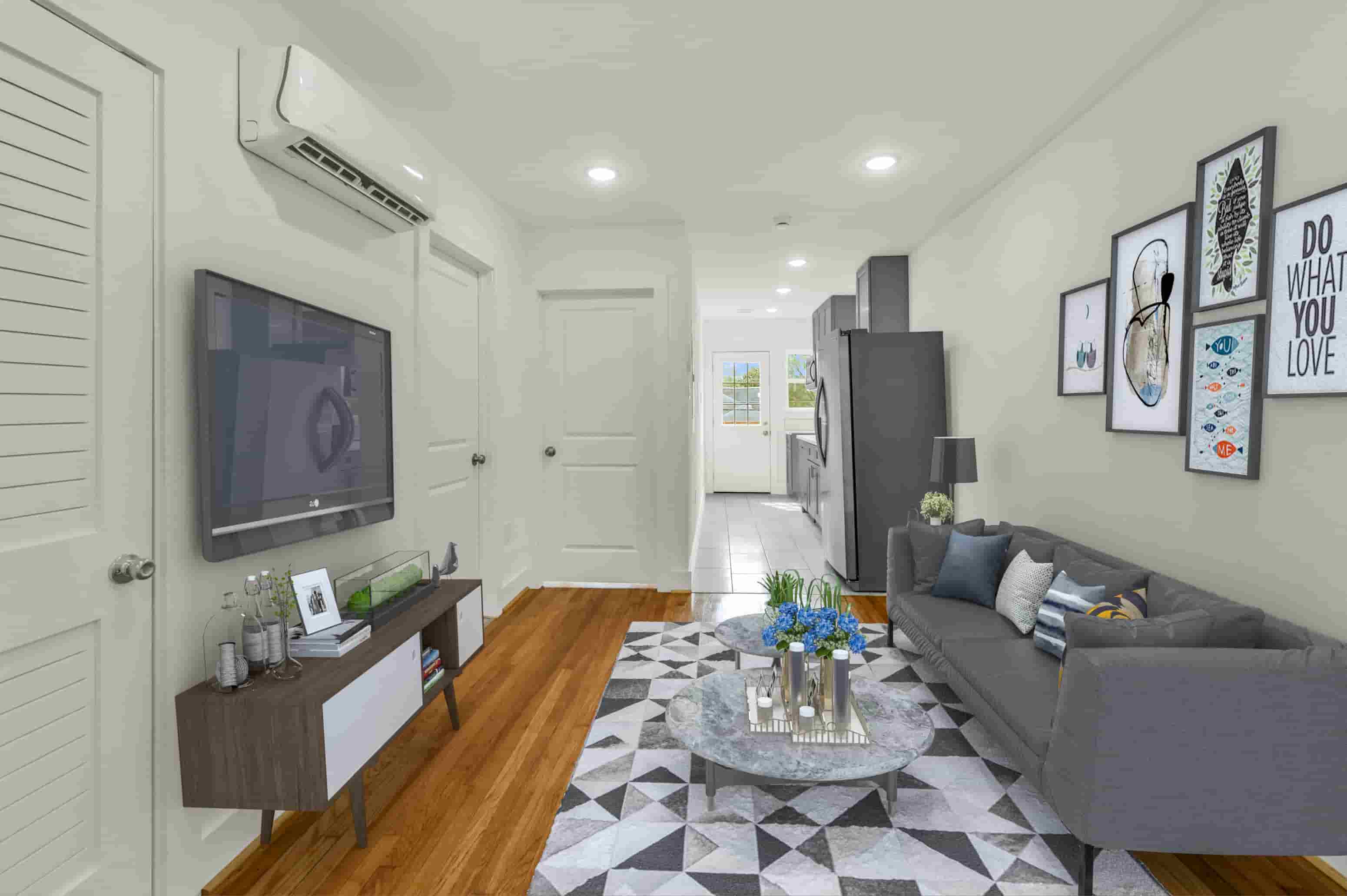 A living room with a grey couch, a coffee table, and a TV on the wall.
