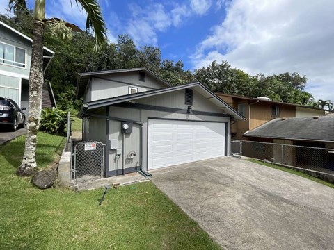A detached garage with a white door is surrounded by a fence and a palm tree.
