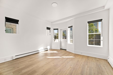 A room with white walls and wooden flooring with a window on the right.