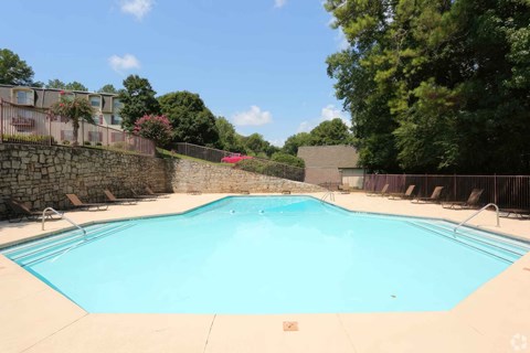 A large swimming pool surrounded by a stone wall and trees.