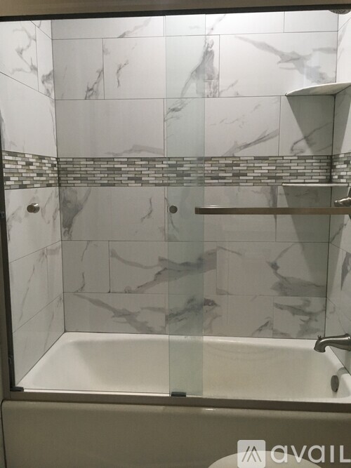 A bathroom with a marble tile wall and a glass shower door.