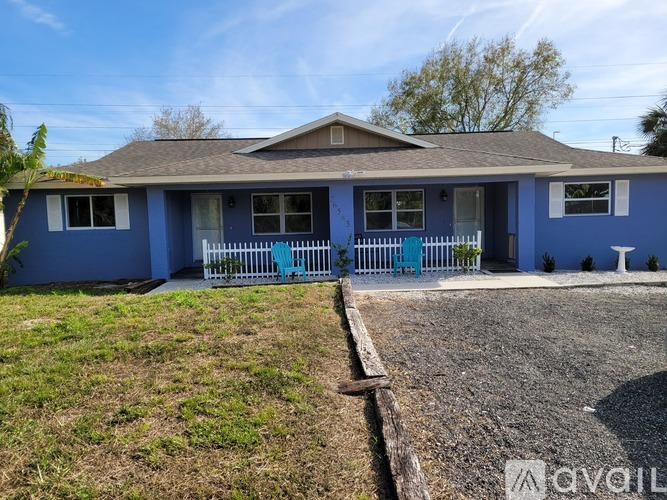 A blue house with a white fence and a gravel driveway.