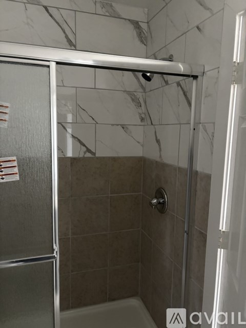 A shower area with a glass door and a marble tile wall.