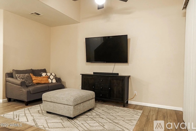 A living room with a grey couch, a grey ottoman, and a black TV on a black cabinet.
