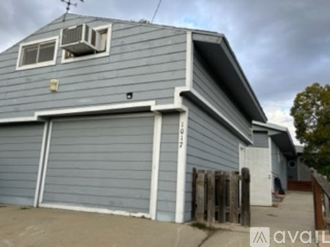 A grey house with a white garage door and a window with an air conditioner unit.