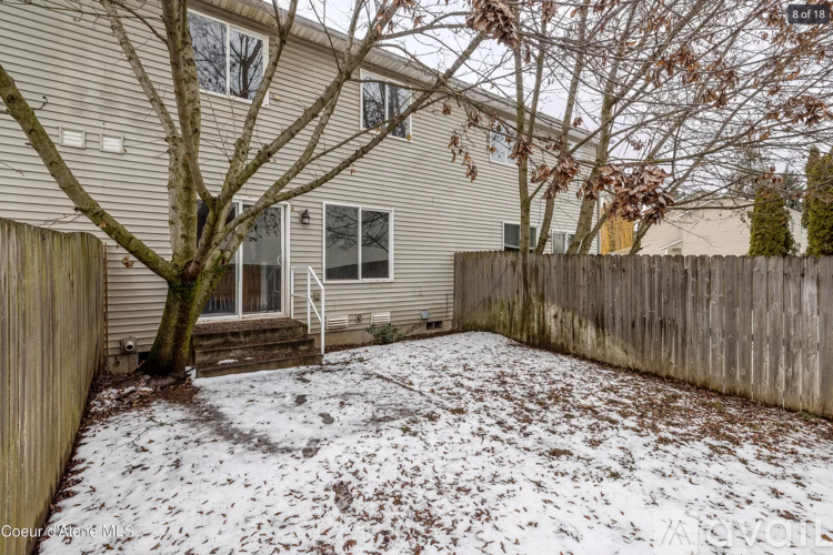 A backyard with a fence and a tree with snow on the ground.