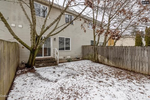 A backyard with a fence and a tree with snow on the ground.