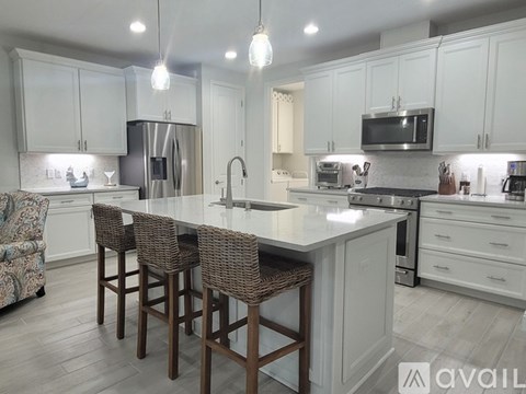 A kitchen with white cabinets and a center island with chairs.