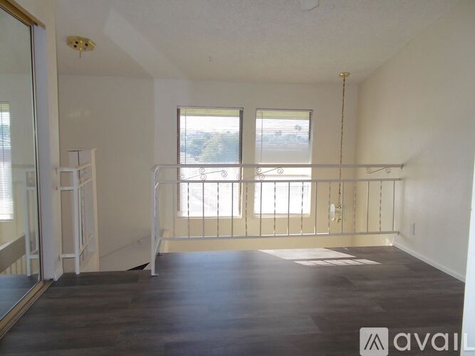 A spacious room with wooden floors and a balcony with a railing.