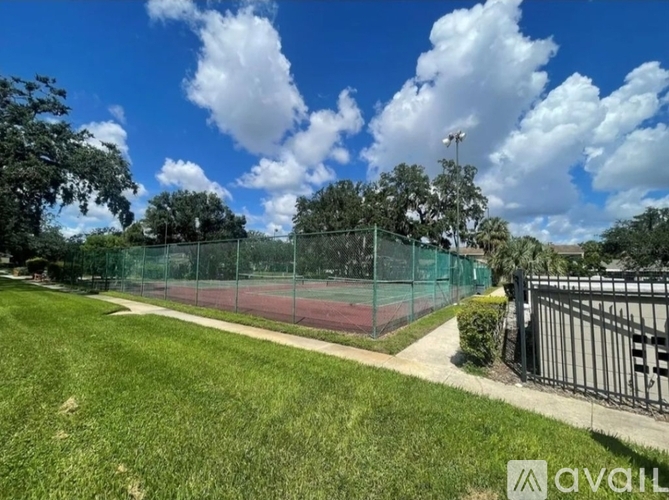 A tennis court is surrounded by a green fence and trees.