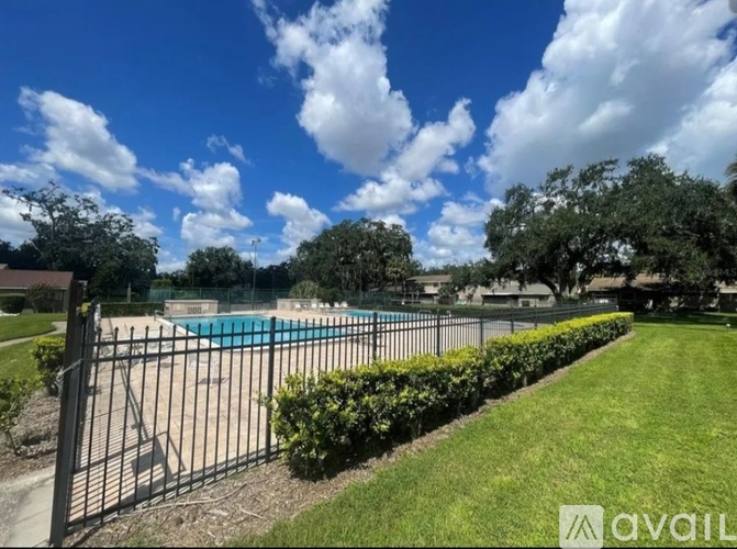 A pool surrounded by a black fence and green bushes under a blue sky with clouds.