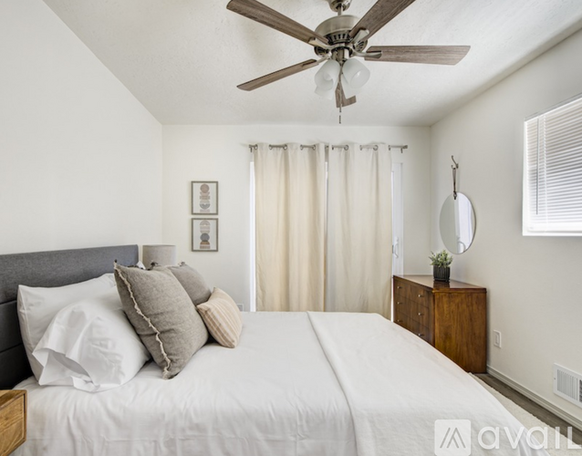 A bedroom with a bed, a ceiling fan, and a nightstand with a plant on it.