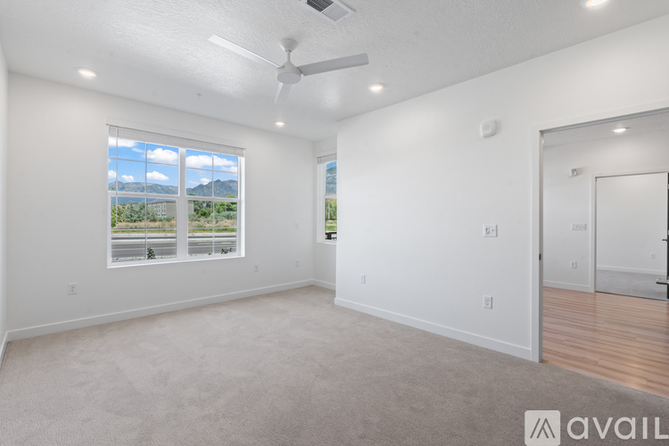 A spacious room with a ceiling fan and a large window overlooking a road.