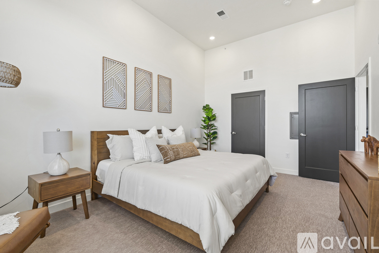 A bedroom with a large bed, a nightstand with a lamp, and a wooden dresser.