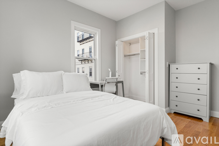 A white bedroom with a large bed, a nightstand, and a dresser.