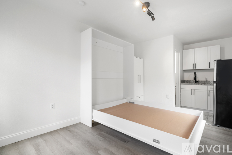 A bedroom with a large bed and a kitchen area in the background.