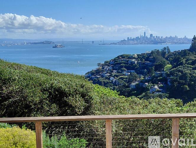 A view of a city skyline from a hill with a wooden fence in the foreground.