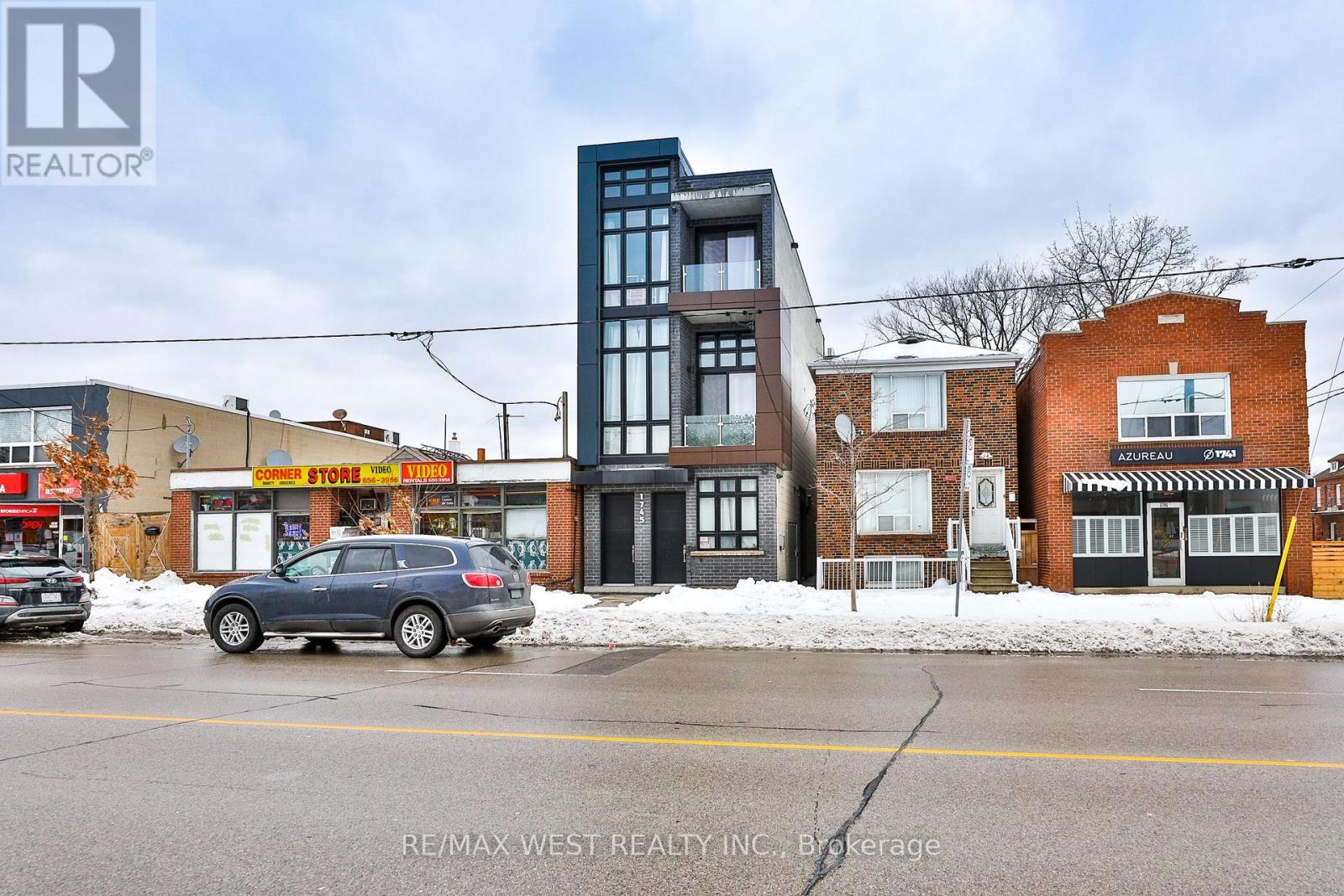 A grey car is parked in front of a building with a sign that says RE/MAX West Realty Inc. Brokerage.