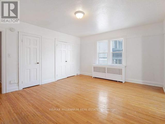 A room with white walls and wooden flooring, with a window and a radiator.