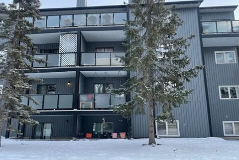 A large grey building with a balcony and a tree in front of it.